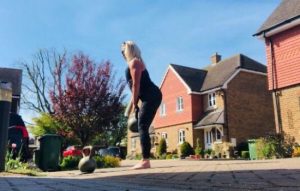 woman lifting kettle bell outside a house